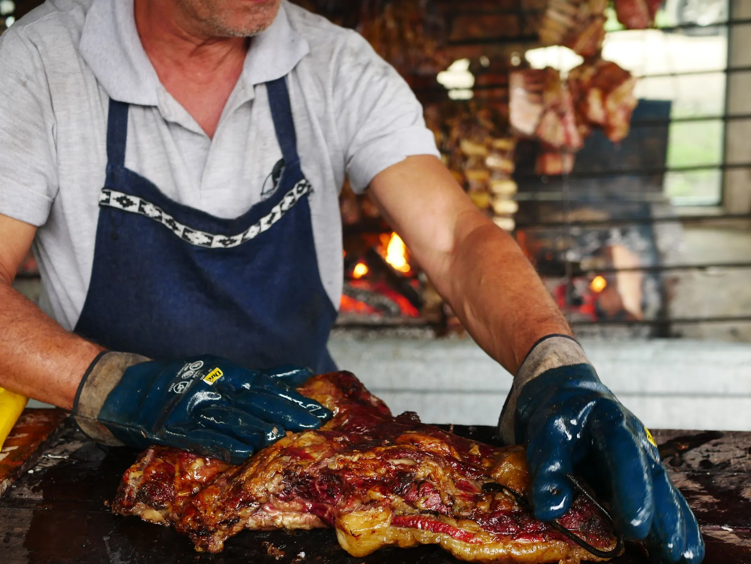 El parrillero preparando una pieza de carne junto al fuego de la parrilla